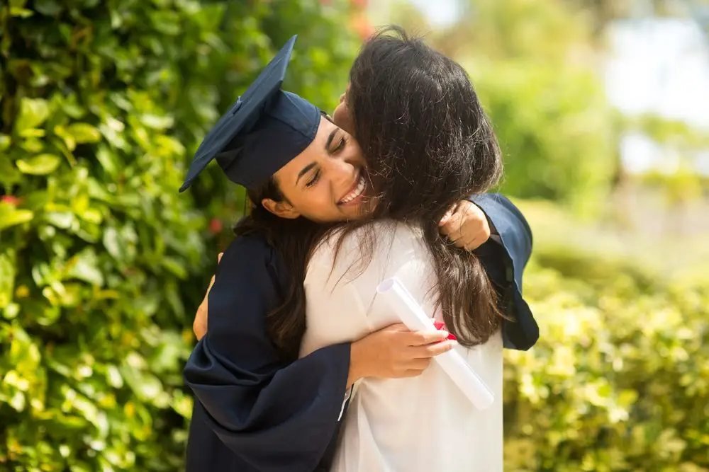 A graduate in cap and gown embracing a family member after her defense