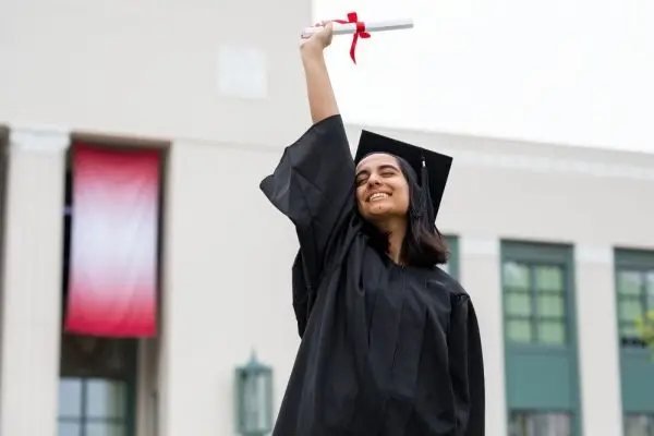 A graduate holding up her diploma outside the campus building